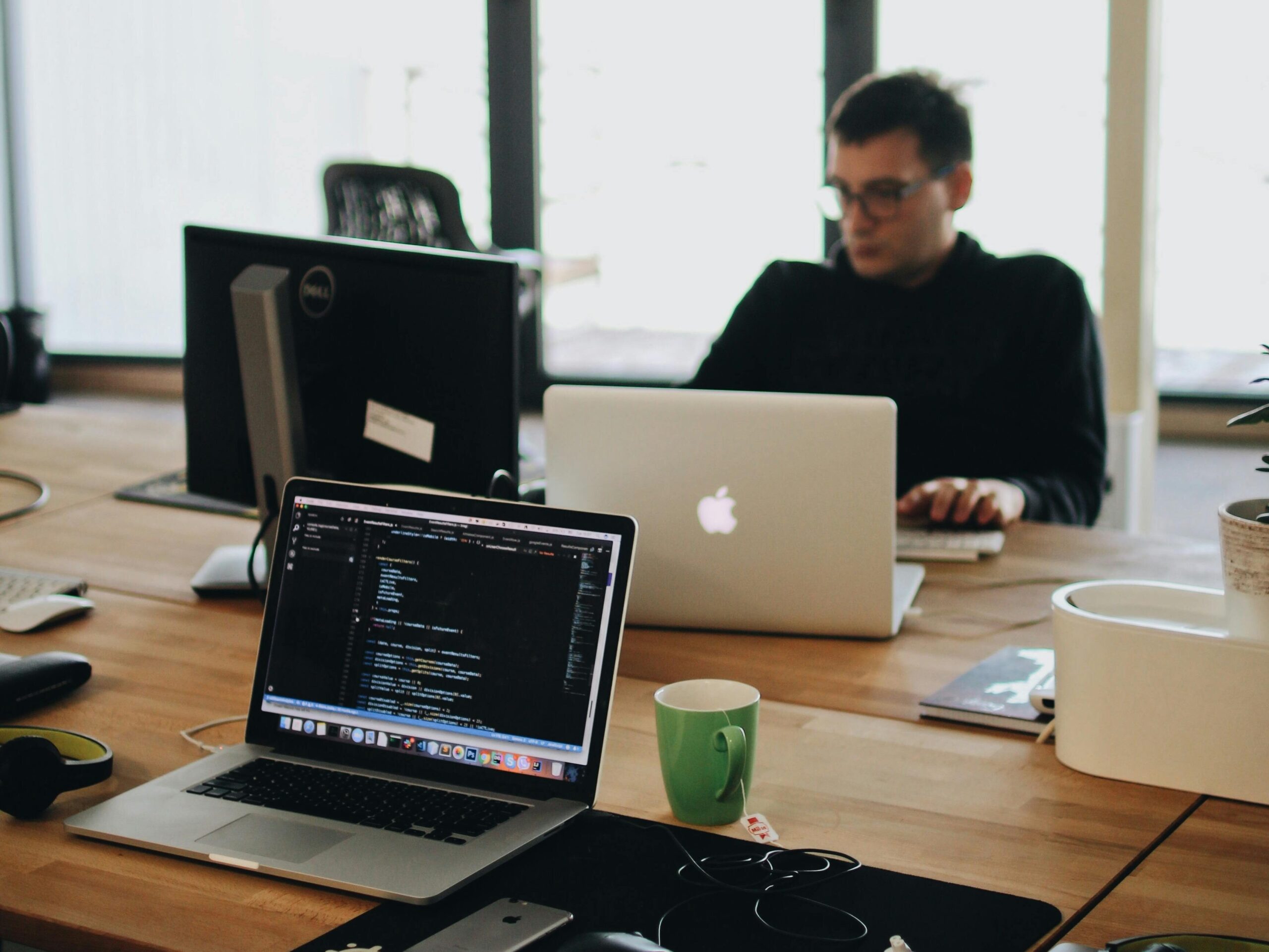 A web developer working on code in a modern office setting with multiple devices.