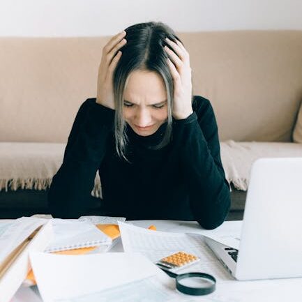 A woman appears stressed and overwhelmed with paperwork at her home desk.